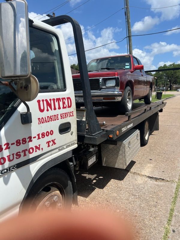 Tow truck carrying a red pickup on a flatbed in a sunny street scene