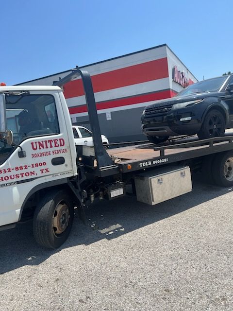 Tow truck hauling a black pickup in front of a United Auto Sales building under a clear blue sky