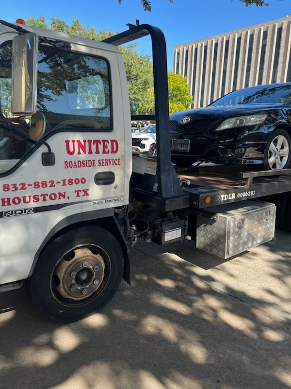 Tow truck loading a black car in a sunlit lot, with “United” signage on the cab.