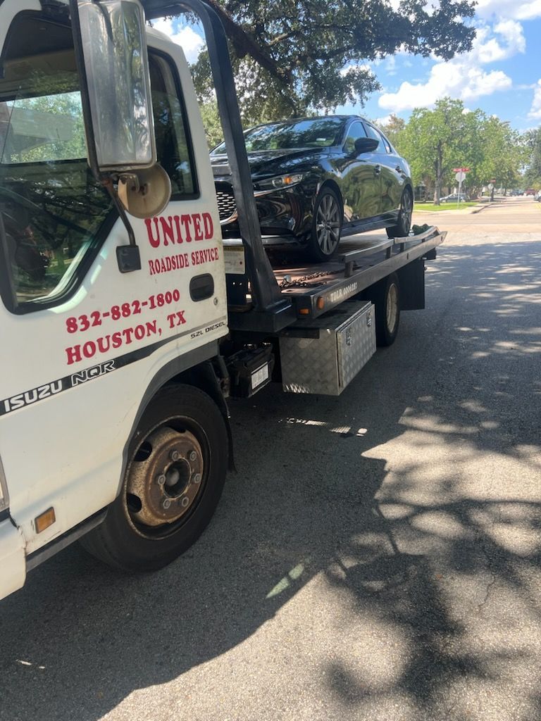 Tow truck carrying a black SUV on a tree-lined street in Houston, Texas