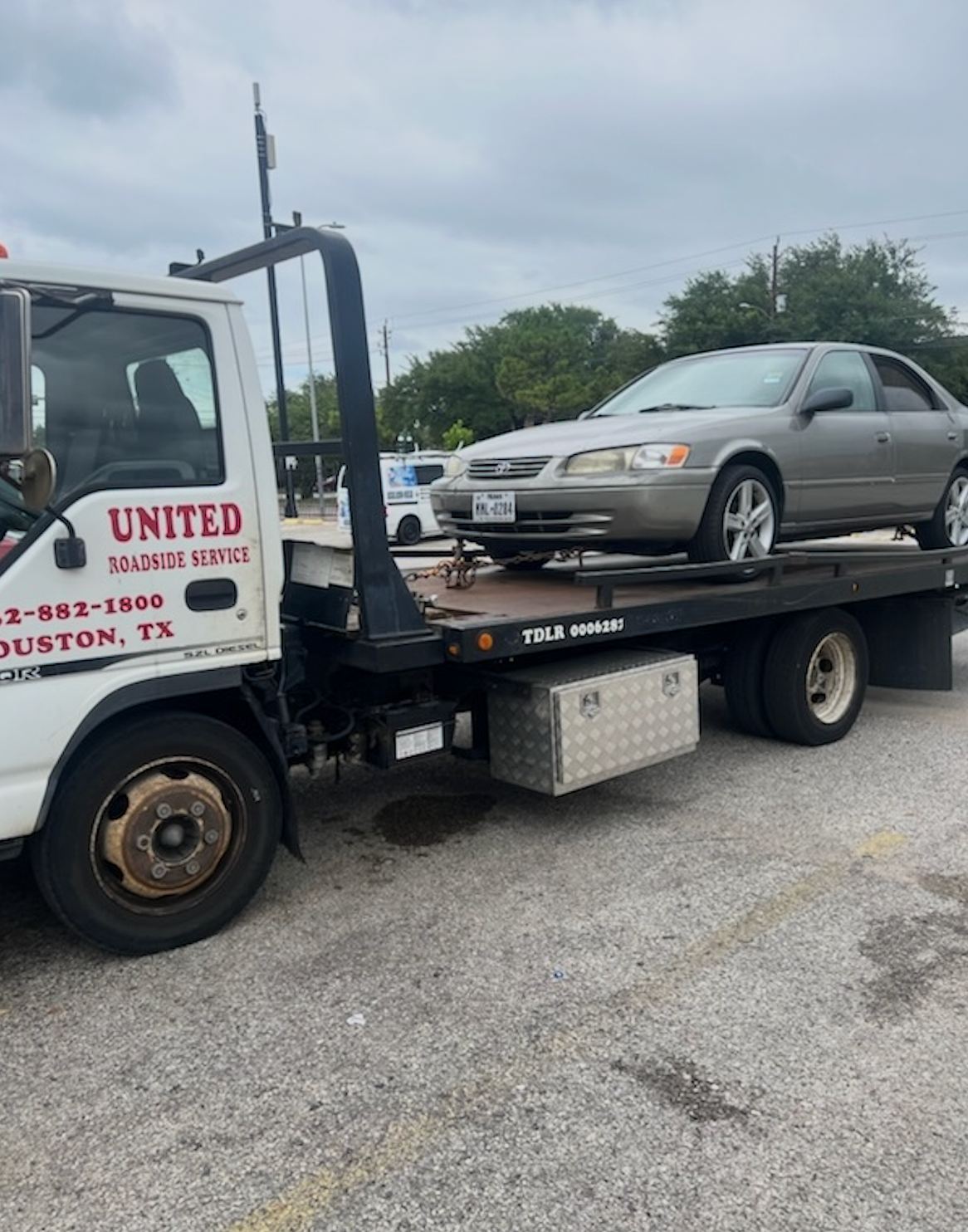 Tow truck carrying a silver sedan in a parking lot under cloudy skies