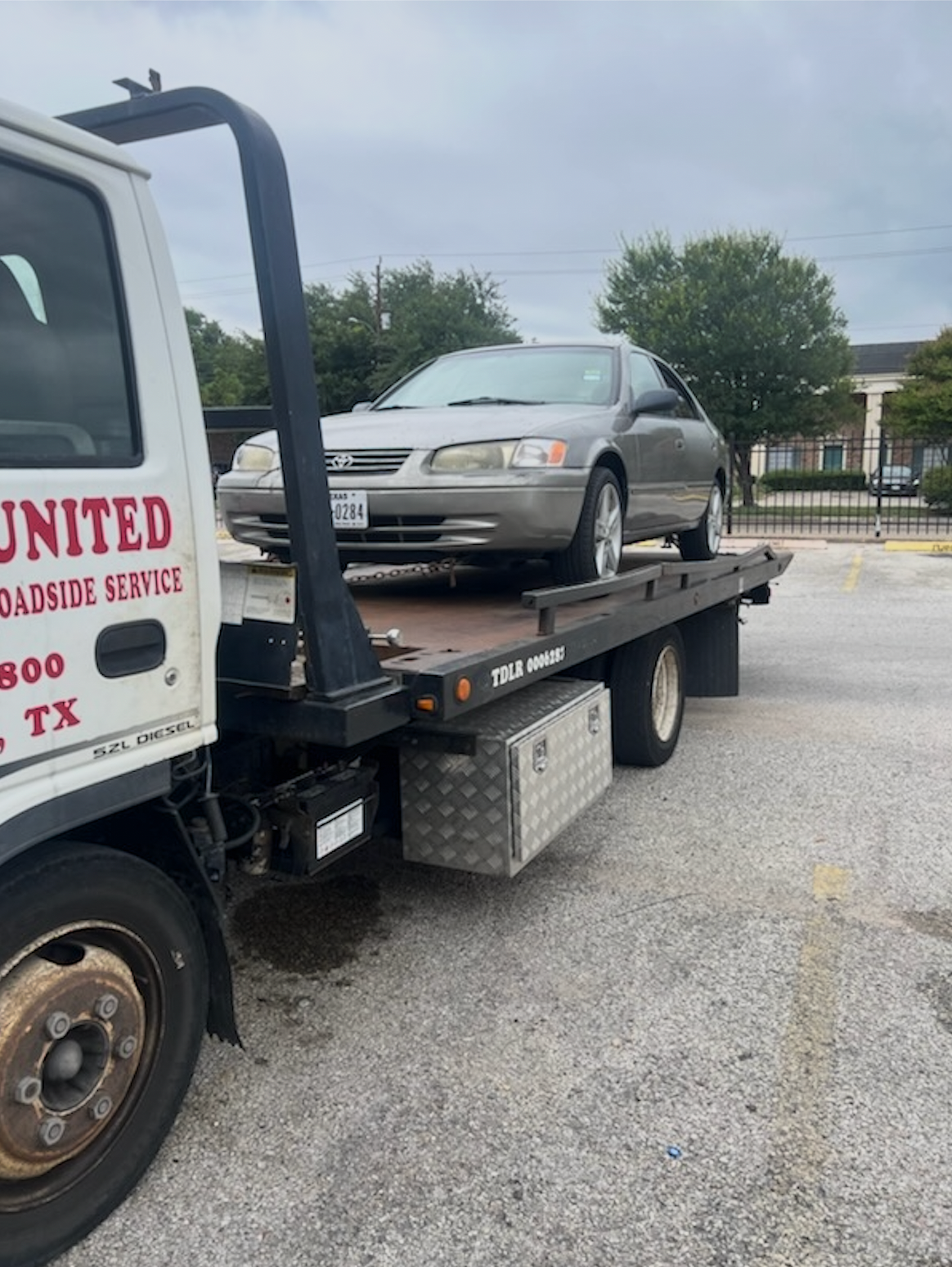 Tow truck carrying a silver sedan in a parking lot under an overcast sky