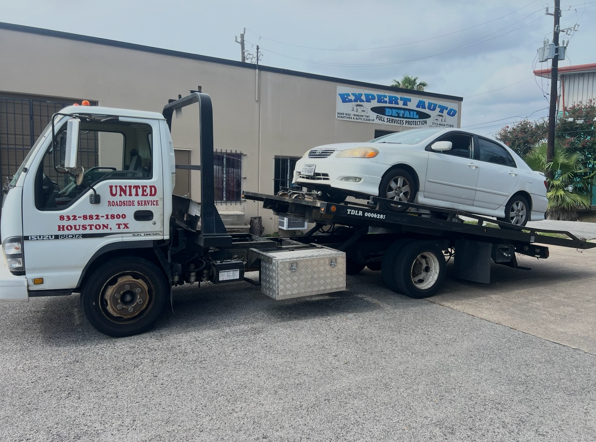 Tow truck loading a white sedan on a flatbed in an industrial lot