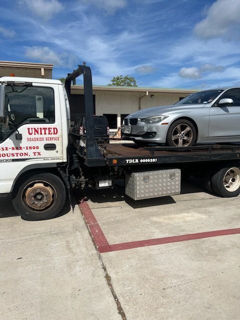 Tow truck carrying a silver sedan in a parking lot under a cloudy sky