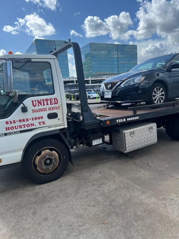 Tow truck hauling a black minivan in front of a glass office building under a cloudy sky