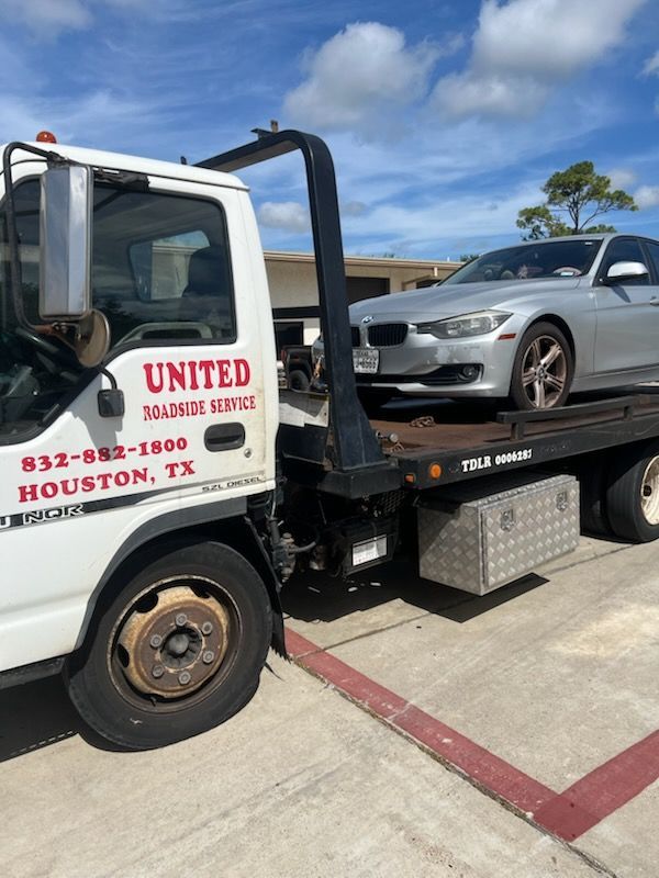 Tow truck loading a silver sedan on a flatbed in a parking lot under a blue sky