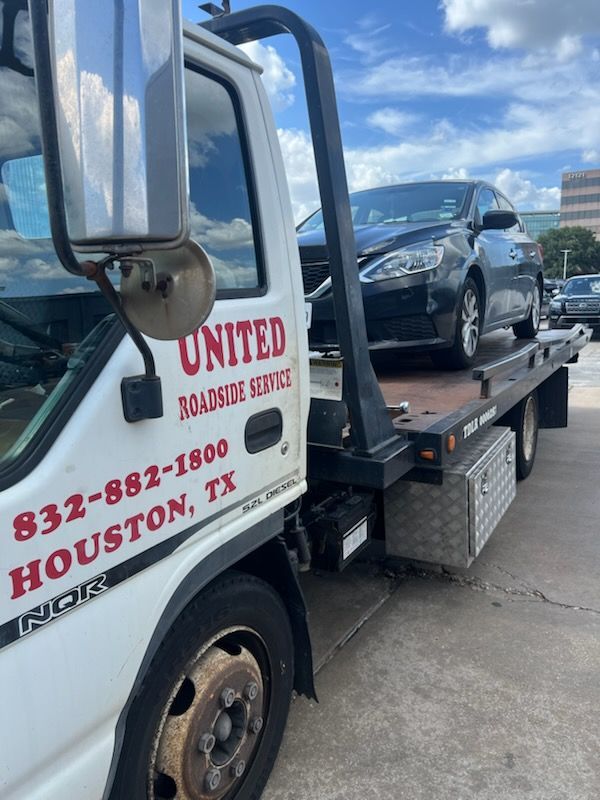 Tow truck carrying a black car, with UNITED towing company lettering on the cab.