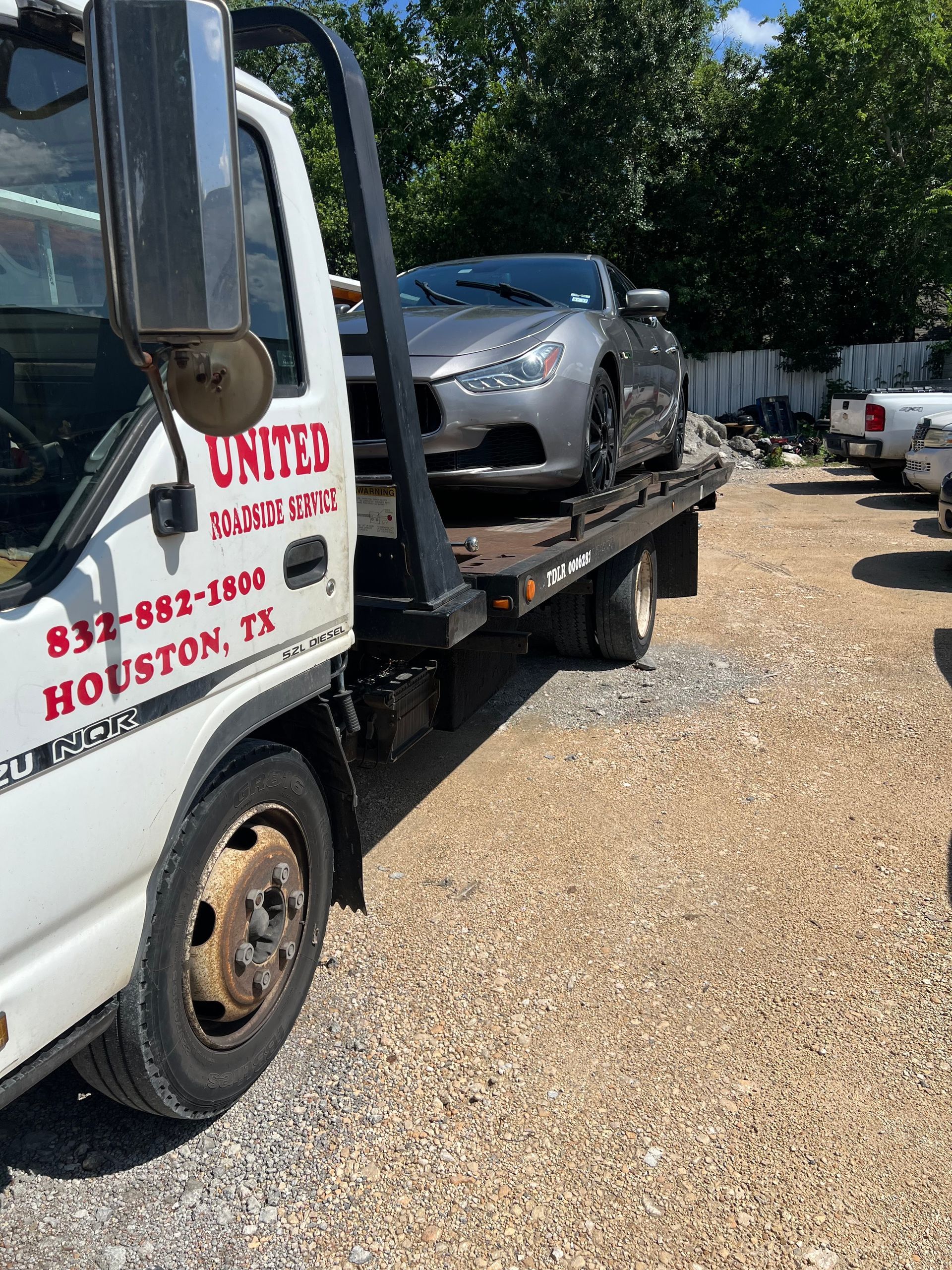 Tow truck carrying a silver car on a gravel lot, with red lettering on the truck door