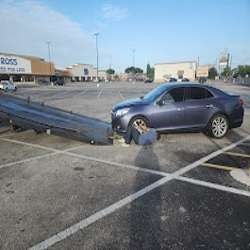Blue sedan hooked to a tow truck in a mostly empty parking lot