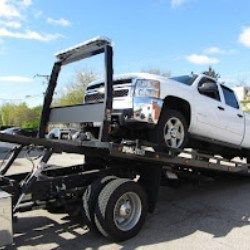 White pickup truck loaded on a flatbed tow truck under a blue sky