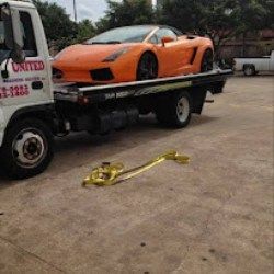 Orange sports car on a flatbed tow truck, with a yellow tow strap on the ground.