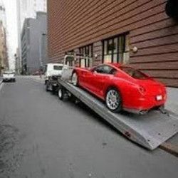 Red sports car on a tow truck ramp on a city street beside a brick building