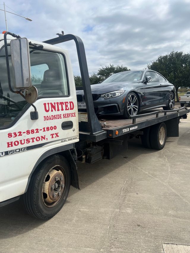 Red tow truck carrying a tan sedan on a highway with traffic cones
