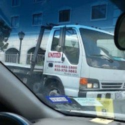 Tow truck with UNITED logo parked beside a building, seen through a car windshield.
