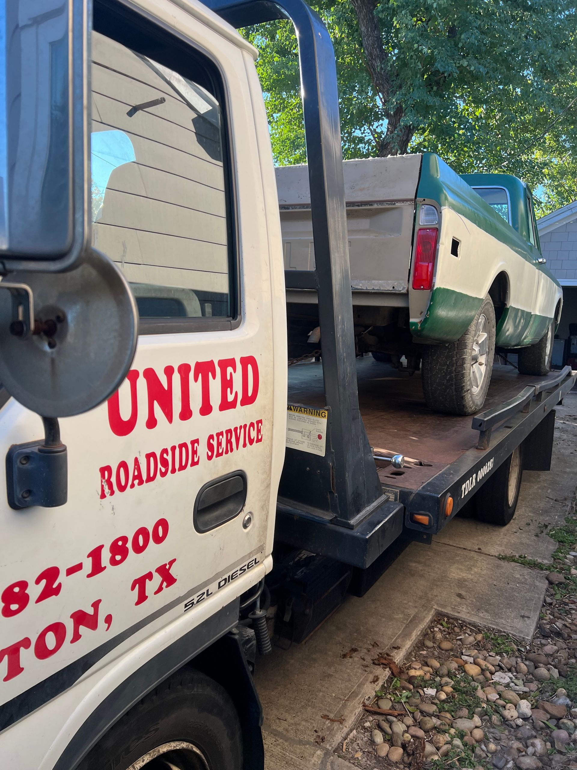 Tow truck loading a white pickup on a flatbed in a roadside setting