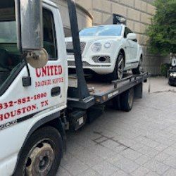 Tow truck loading a white car on a flatbed in an urban alley
