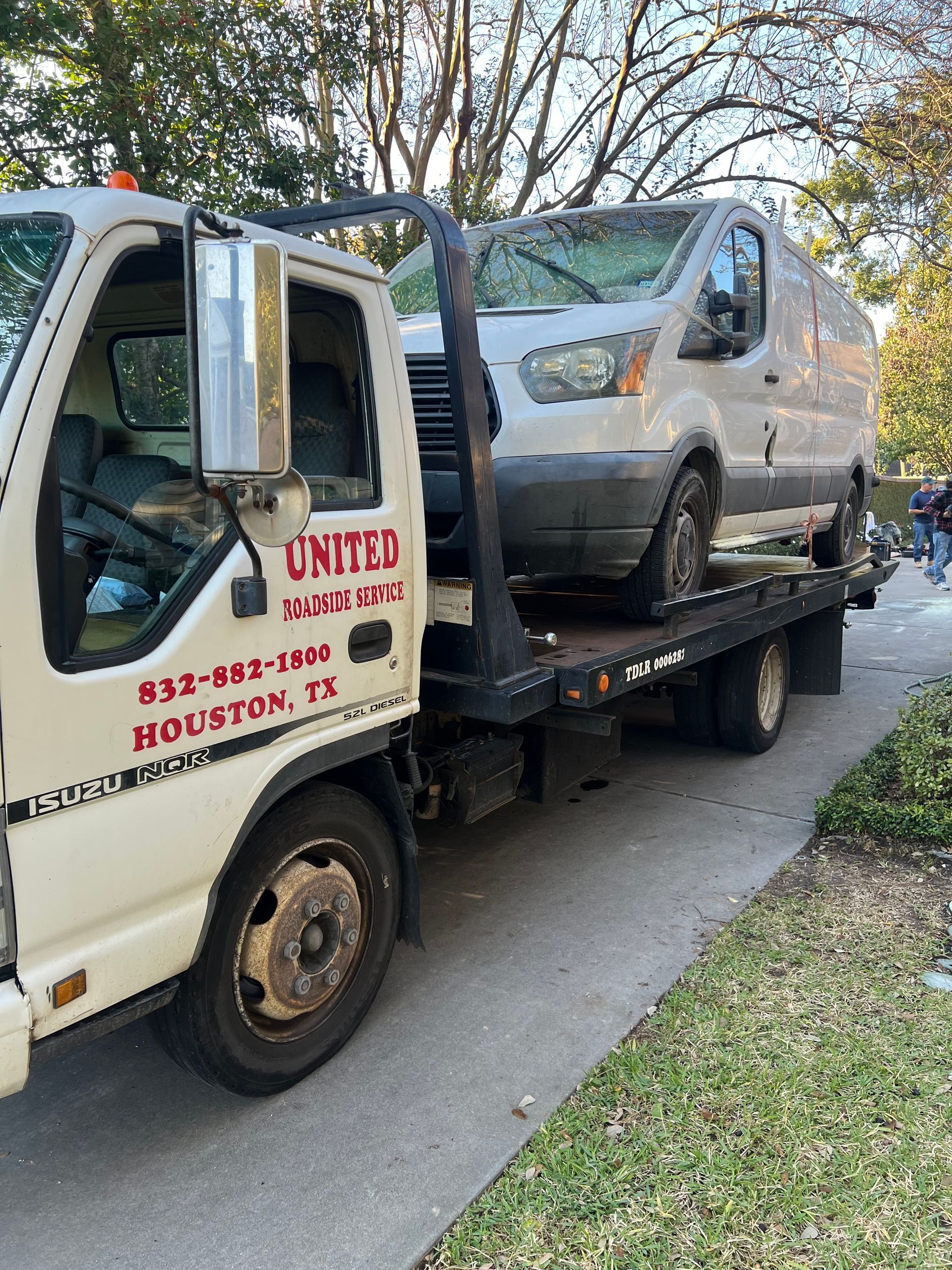 Tow truck hauling a silver van on a flatbed along a residential street.