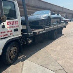 Black sports car on a tow truck in a sunny industrial lot