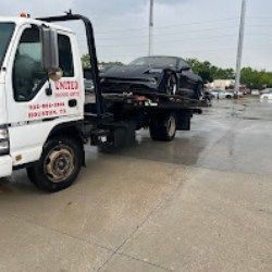 Tow truck hauling a black sedan on a wet roadside in a parking lot