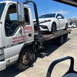 White sports car on a tow truck in a sunny parking lot