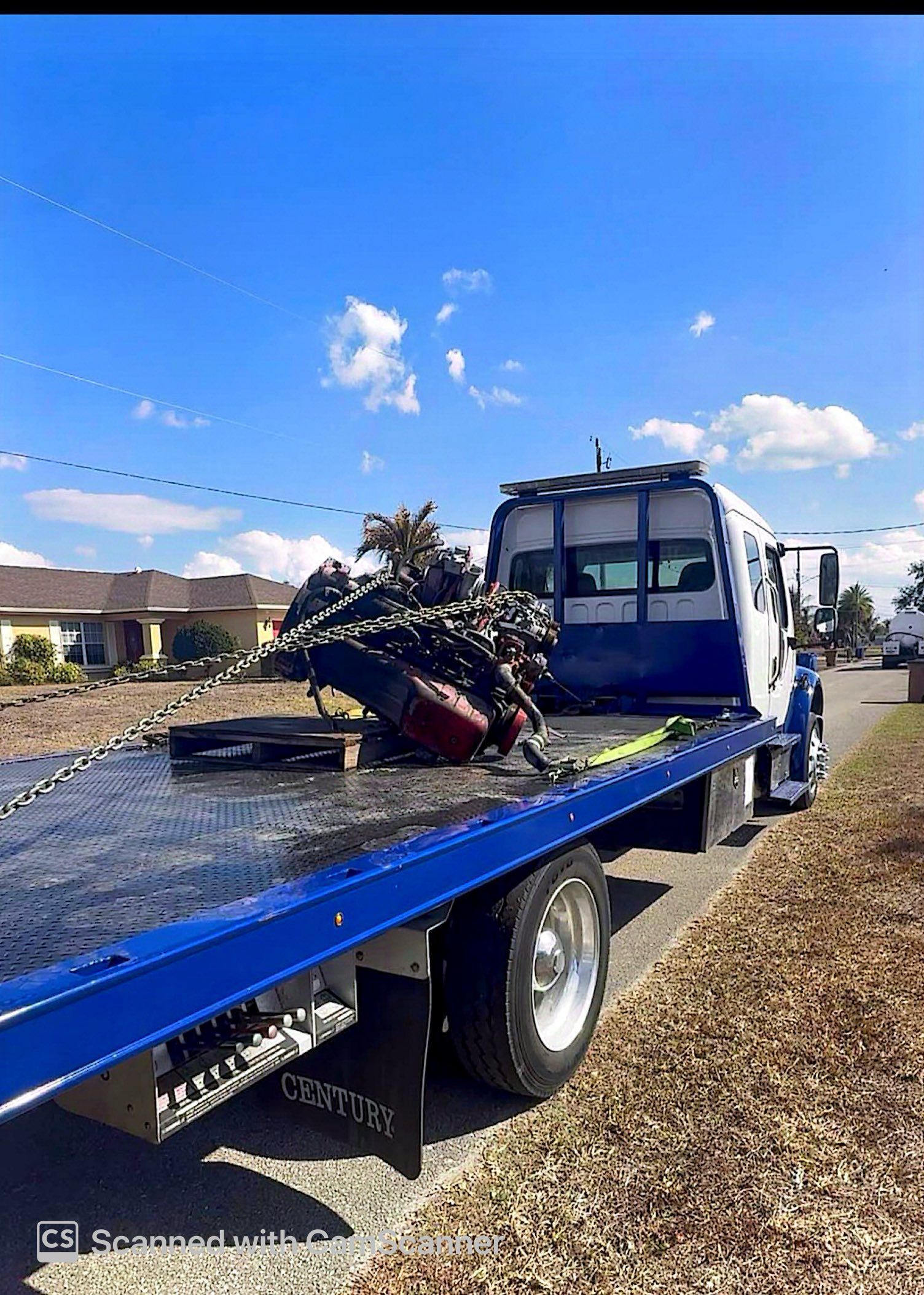 Blue flatbed tow truck carrying a damaged motorcycle on a sunny roadside