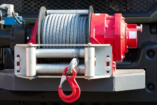 Red winch with steel cable and hook mounted on a vehicle bumper