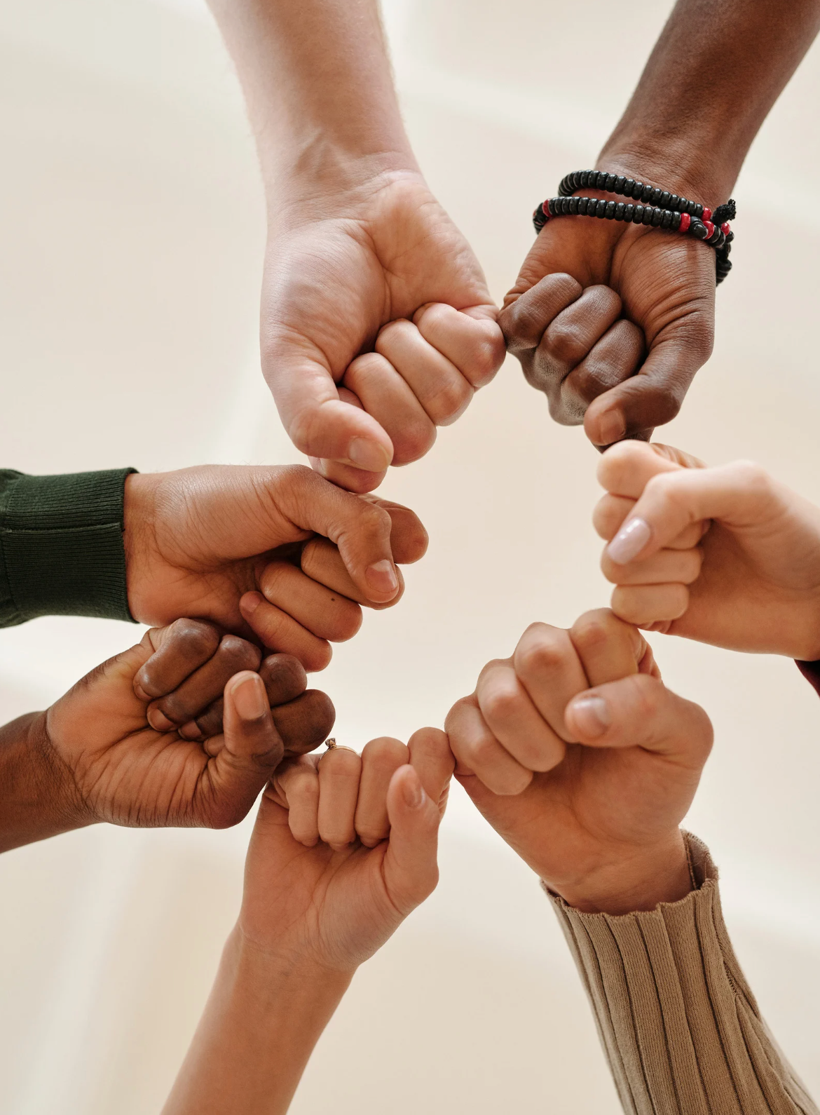 Hands of various skin tones form a circle, fists touching, showing solidarity.