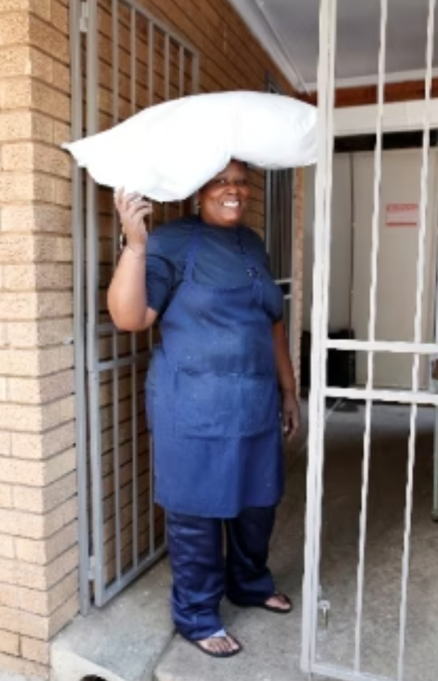 Person in blue uniform balances a white pillow on their head, smiling, standing in doorway.