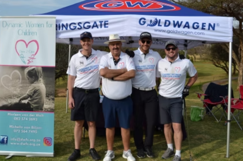 Four men in golf attire pose under a branded canopy.