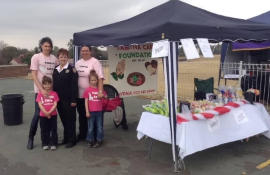 People at a Tabitha Cares Foundation stall selling produce. Several people wear pink shirts.