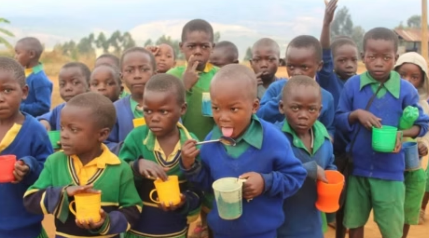 Group of children in school uniforms hold cups, likely drinking outside.