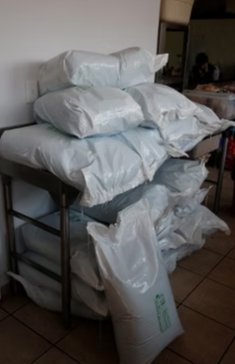Bags of goods stacked on a metal shelf, possibly in a commercial kitchen or storage area.