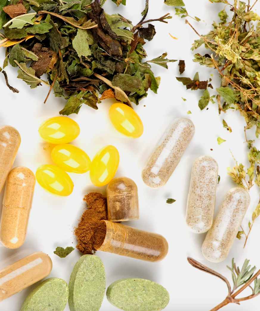 Assorted herbal supplements and pills, with dried herbs and capsules, on a white surface.