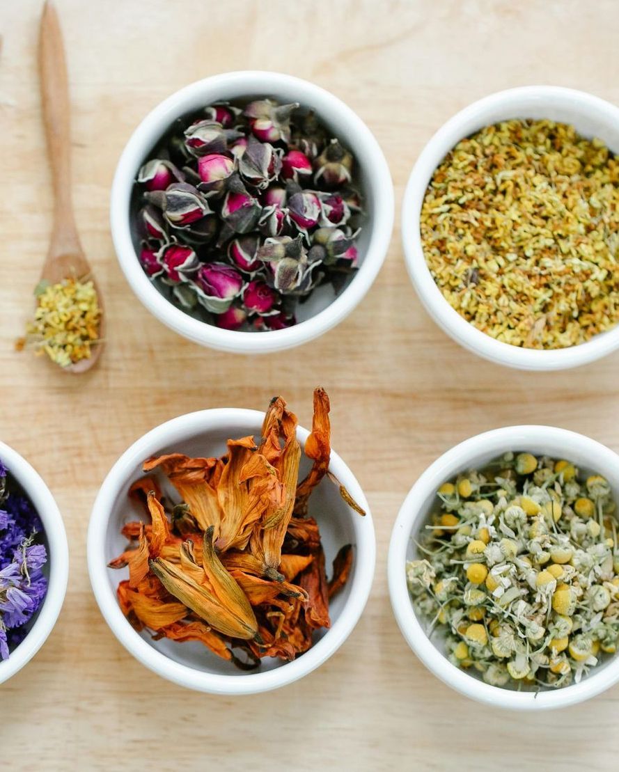 Dried herbs and flowers in white bowls on a wooden surface, ready for tea.