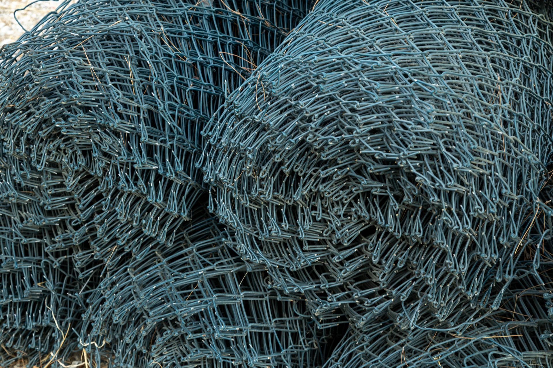 Dark green rolls of woven chain-link wire mesh rest on a construction site.