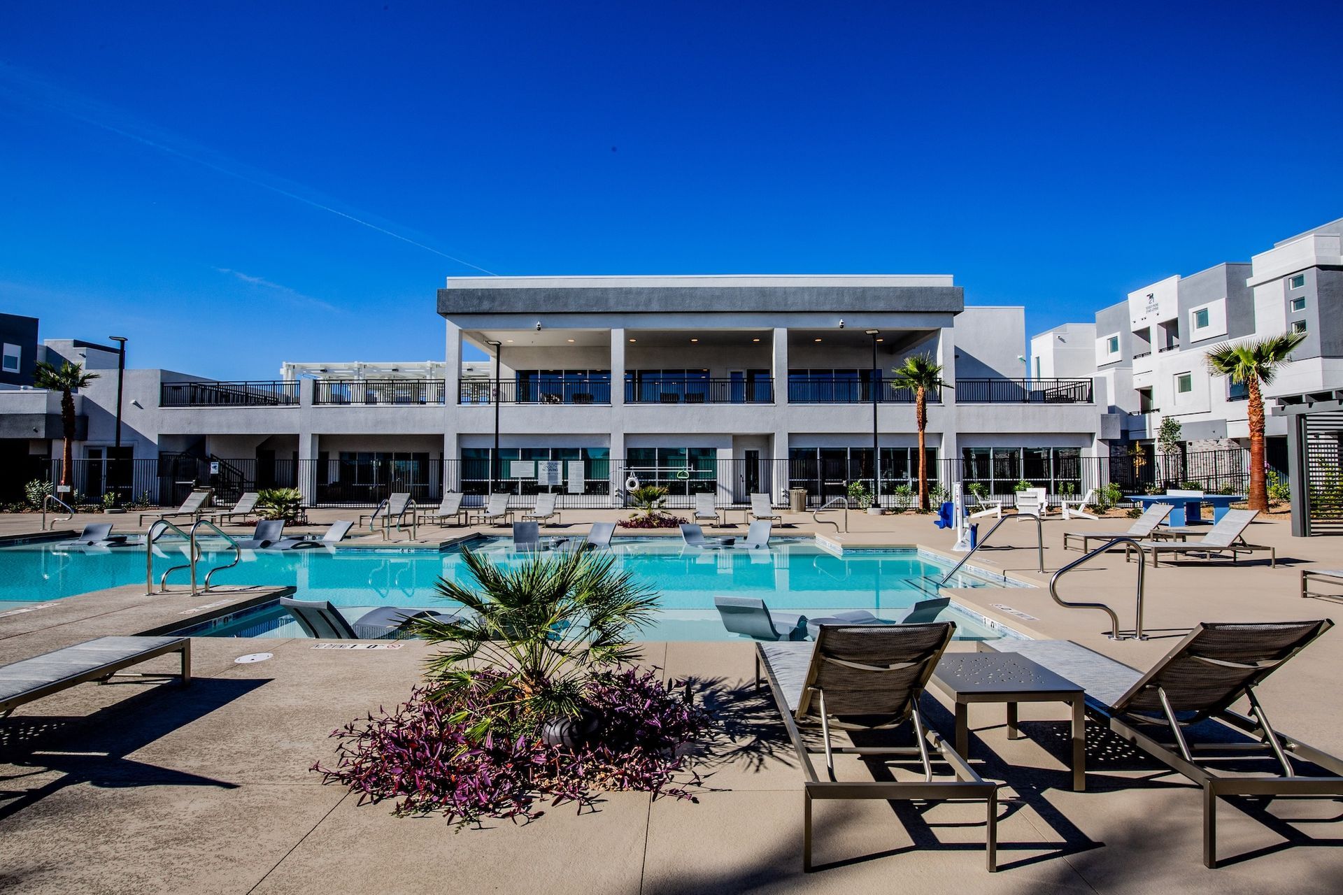 Swimming pool with lounge chairs in front of a modern building under a blue sky.