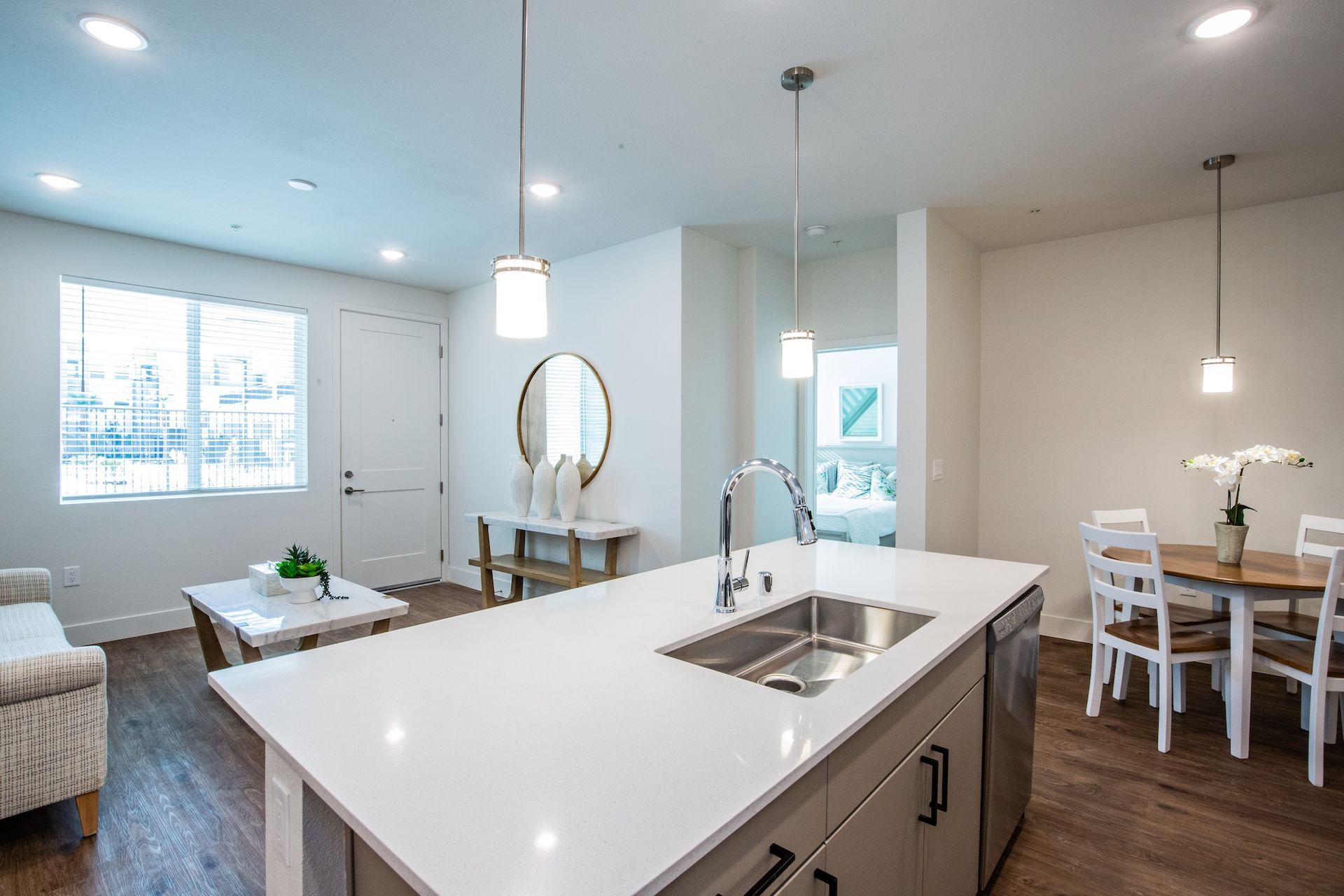 Open-concept kitchen and living area with a large island, white walls, and pendant lights.