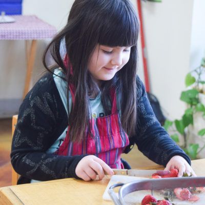 Young person slicing strawberries on a table, wearing an apron, smiling.
