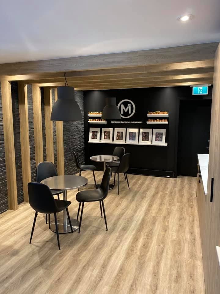 A cafe interior with tables, chairs, and a black wall with a logo and framed pictures.