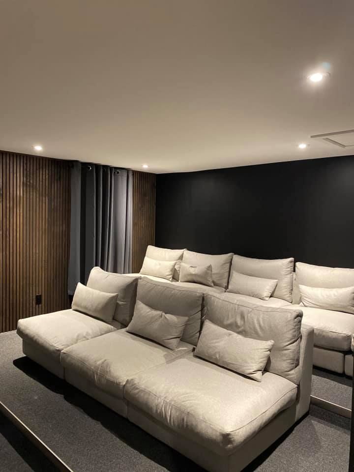 Rows of light gray seating in a home theater. Dark wall, wood paneling, and gray carpet.