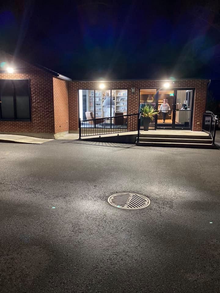 Brick building entrance at night with illuminated doorway, ramp, and manhole cover on asphalt.