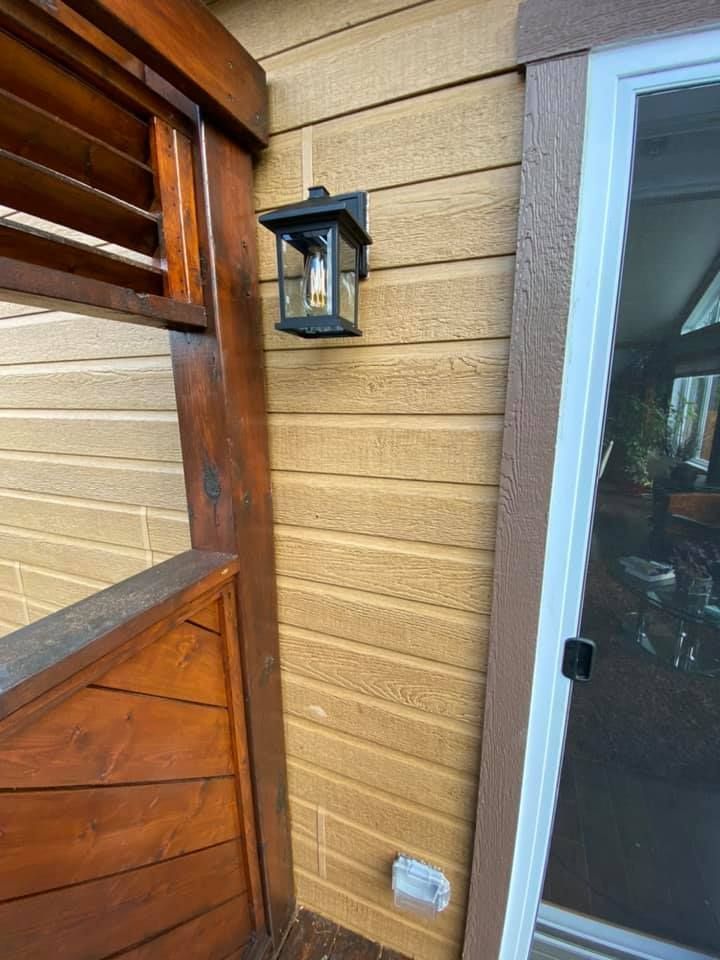 Black outdoor lantern on tan siding, next to a glass door.