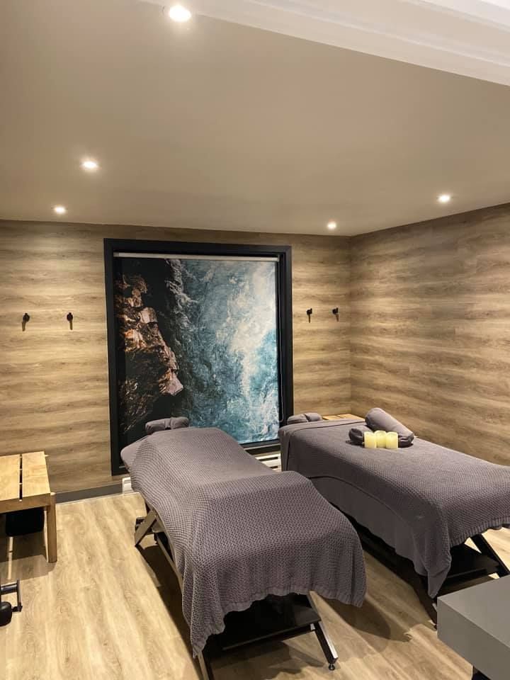 Two massage tables in a spa room, wood-look walls, art of ocean waves.