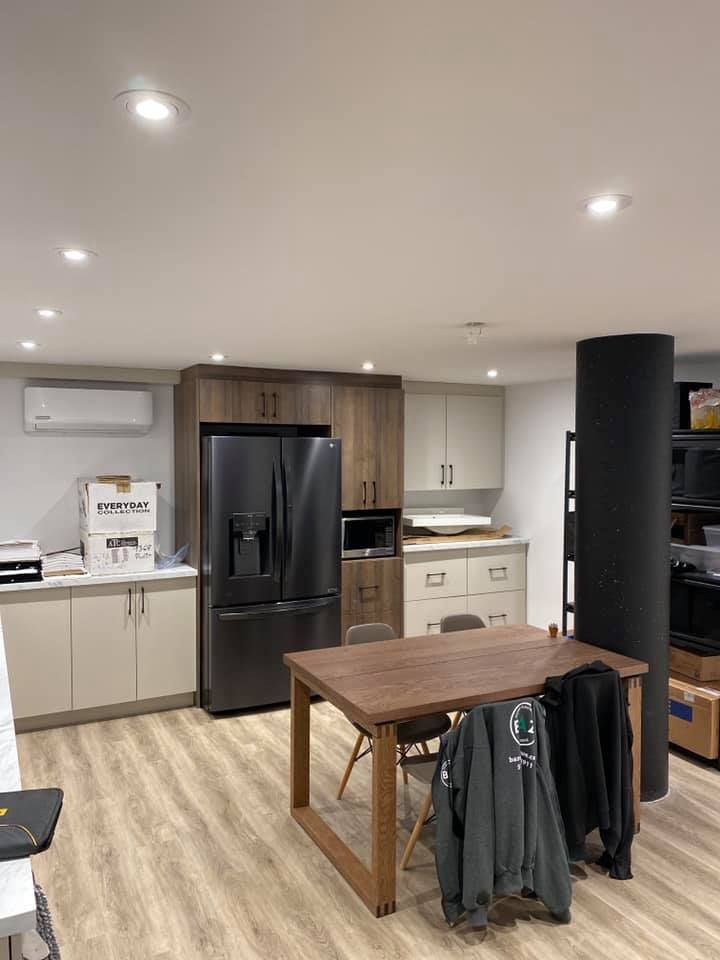 Kitchen area with cabinets, refrigerator, table, and dark column. Beige, brown, and gray colors.