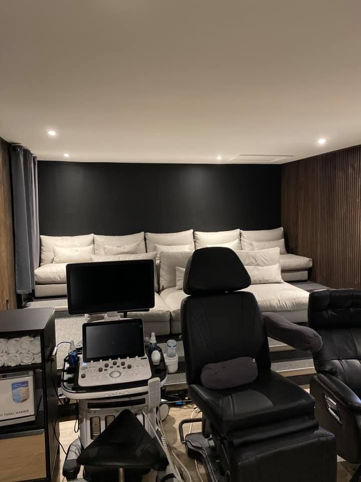 Ultrasound room with a black wall, sofa seating, medical equipment, and a patient chair.