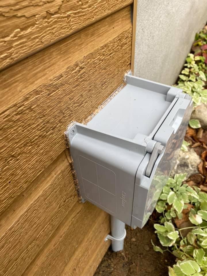 Gray electrical box mounted on a brown wooden wall with a white pipe leading down.