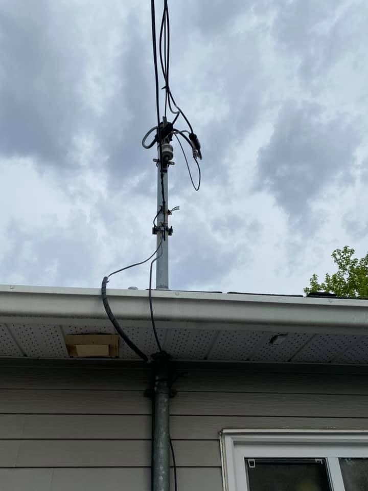 Telephone pole mounted on a roof, cables connecting to overhead lines against a cloudy sky.