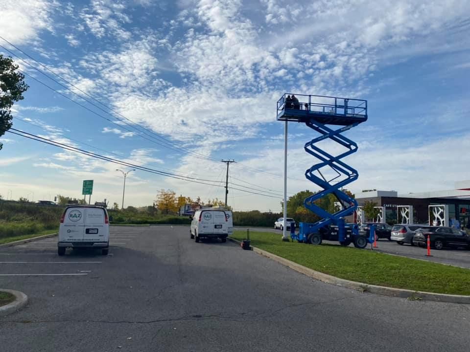 Blue scissor lift with workers near a white van and a McDonald's building on a cloudy day.