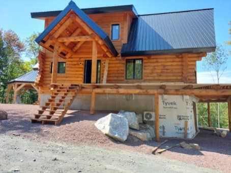 Wooden cabin with black roof and porch. Steps lead up to the front door. Large rocks in front.