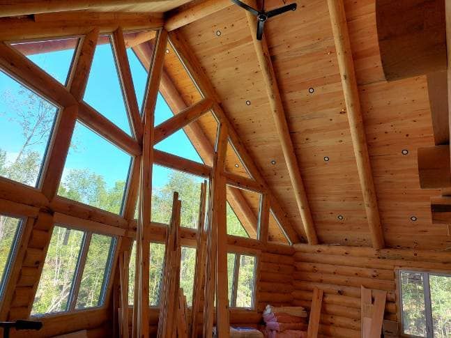 Interior of log cabin with large triangular windows showing a bright blue sky.